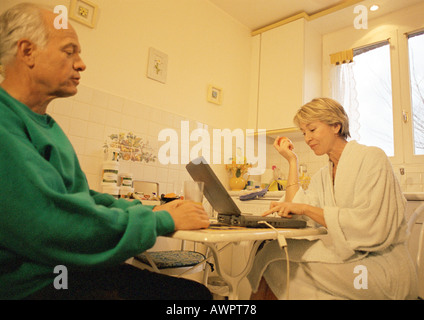 Mature couple in kitchen, woman using laptop, man holding glass Stock Photo