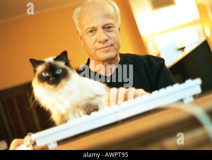 Mature man with Persian cat and hand on computer keyboard, looking into camera, portrait Stock Photo