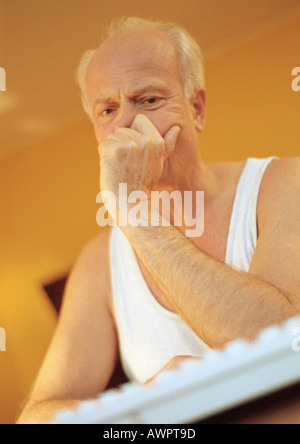 Mature man, hand to face, with computer keyboard, portrait. Stock Photo
