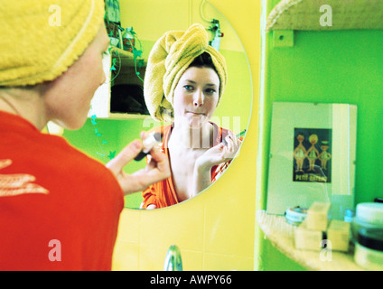 Young woman putting on make-up, focus on reflection in mirror. Stock Photo