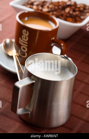 Cannikin with milk froth and a cup of coffe in the background Stock Photo