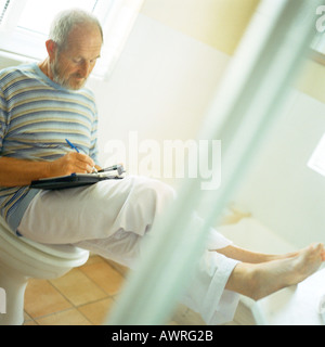 Man sitting on toilet, writing with feet up Stock Photo