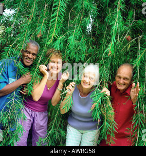 Four people standing side by side under branches, smiling Stock Photo