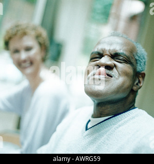 Mature man sticking out tongue, woman smiling in background Stock Photo