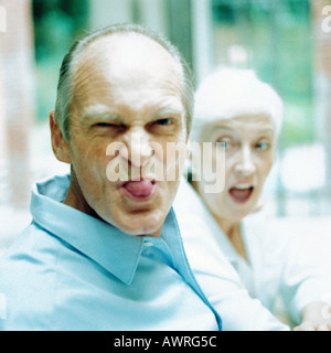 Mature man sticking out tongue, woman in background Stock Photo