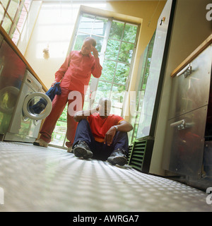 Man sitting on floor, other man taking garment out of washer Stock Photo