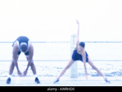 Couple stretching, sea in background, blurred. Stock Photo