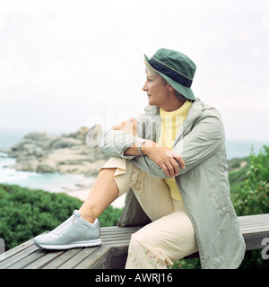 Mature woman sitting on beach, looking out to sea, side view, portrait Stock Photo