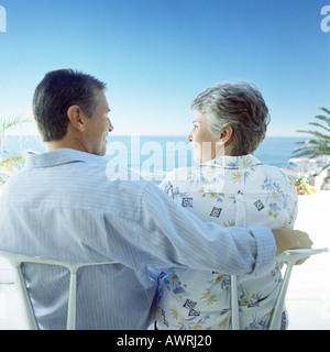 Mature couple sitting on beach, man's arm around woman, rear view Stock Photo