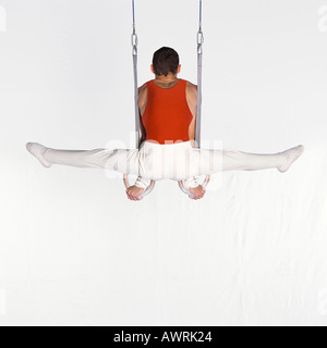 Male gymnast performing on rings, rear view Stock Photo