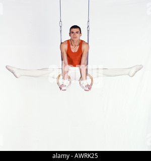 Male gymnast performing on rings, looking at camera Stock Photo