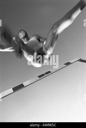 male athlete jumping hurdle, low angle view, blurred motion, b&w Stock Photo