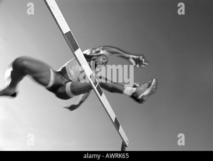 Male athlete jumping hurdle, low angle view, blurred motion, b&w Stock Photo