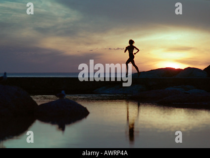 Woman running near water at sunset, silhouette Stock Photo