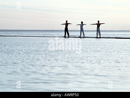 Three people exercising by the sea Stock Photo