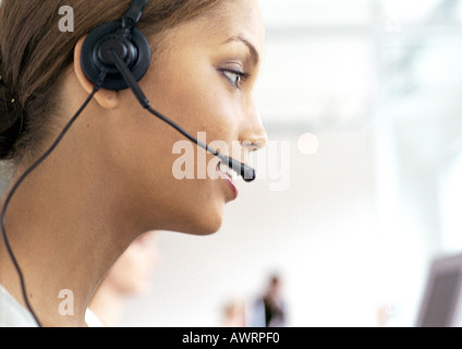 Woman wearing headset in office, side view, close-up Stock Photo