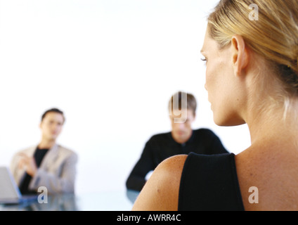 Woman sitting across from two men in office, rear view Stock Photo