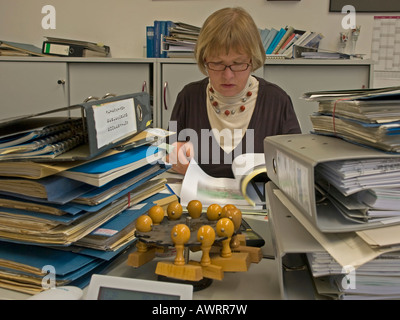 middle aged woman working in bureau checking lot of folders and documents working in bureaucracy Stock Photo
