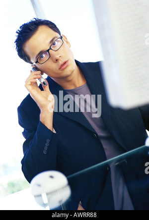 Businessman sitting at computer, using cell phone Stock Photo