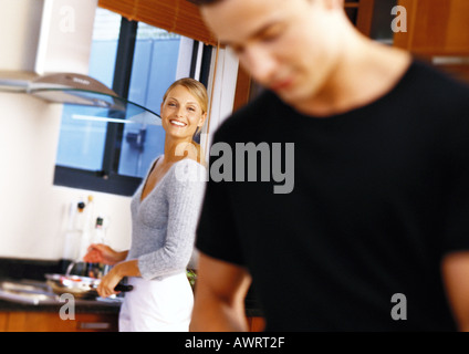 Woman in kitchen, smiling toward man in blurred foreground Stock Photo