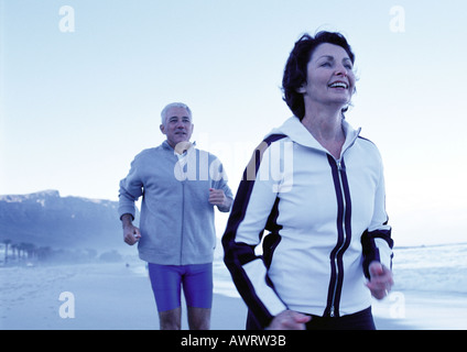 Mature man and woman running on beach Stock Photo