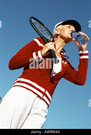 Mature woman holding tennis racket and drinking from bottle of water, low angle view Stock Photo
