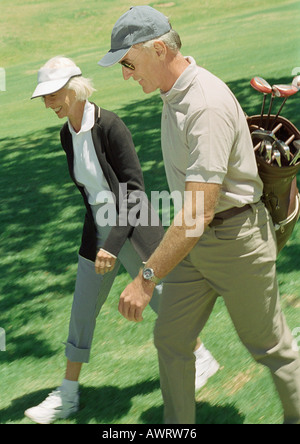 Mature man and woman on green, man carrying golf clubs Stock Photo