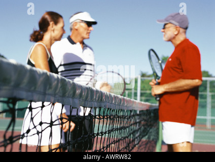 Three mature tennis players on court, side view Stock Photo