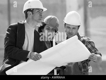 Two men and woman with hard hats examining blueprints, b&w Stock Photo