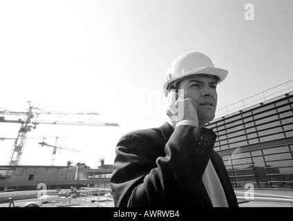 Man in hard hat using cell phone, close-up, in front of construction sight, b&w