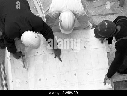 Three people with hard hats, examining blueprint, elevated view, b&w Stock Photo