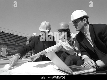 Three people with hard hats examining blueprints, b&w Stock Photo