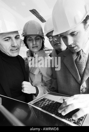 Four people wearing hard hats, one using laptop computer, b&w Stock Photo