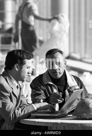 Three men in construction site, one using laptop computer, b&w Stock Photo