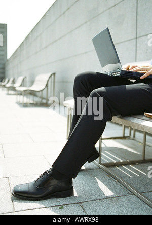 Man on bench with laptop computer on knees, close-up Stock Photo