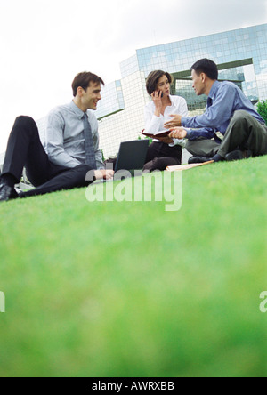 Three people sitting on grass, building in background Stock Photo