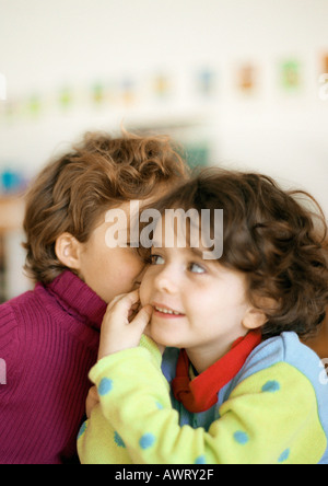 Two children, one whispering to the other Stock Photo