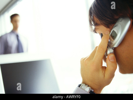 Businessman on cell phone facing computer, side view, close-up Stock Photo