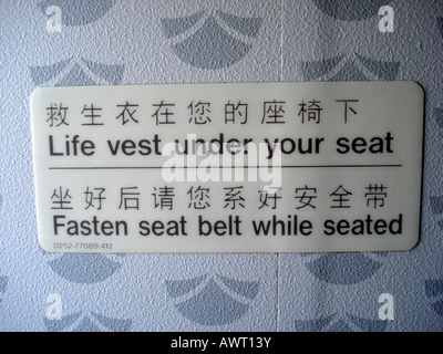 Advisory sign in chinese and english on back of aircraft seat life vest under your seat and fasten seat belt while seated Stock Photo