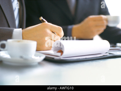 Businessman writing near businessman holding cup Stock Photo