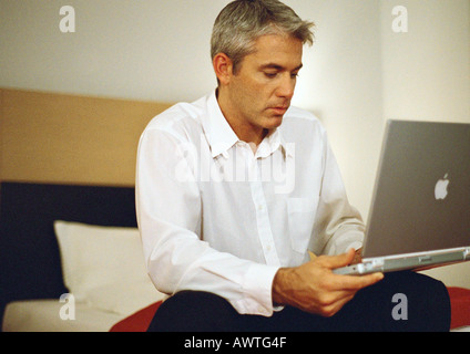 Businessman sitting on bed using laptop Stock Photo