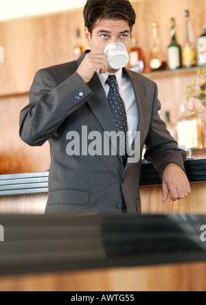 Businessman standing at bar, drinking out of coffee cup Stock Photo