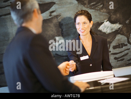 Woman behind counter smiling, handing object to man Stock Photo