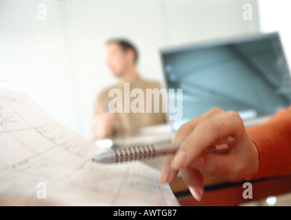 Woman's hand holding pen over agenda, man blurred in background Stock Photo