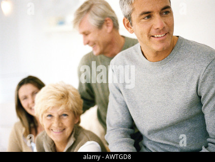 Man looking away, waist up, partial view, three adults smiling in background Stock Photo