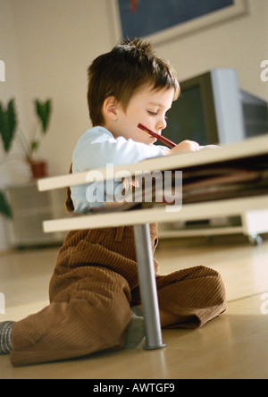 Young boy sitting on floor behind coffee table, drawing, in living room setting, tilt Stock Photo
