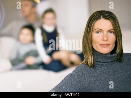 Woman in foreground, head and shoulders, man and two children blurred in background, on sofa Stock Photo