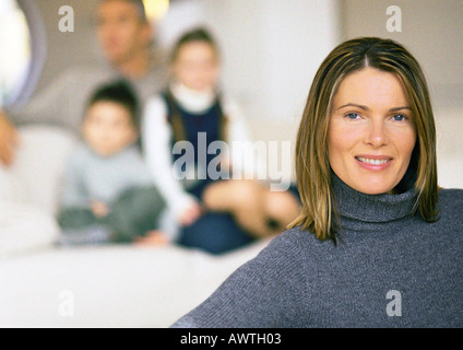 Family, mother in foreground, husband and two children blurred in background, close up Stock Photo