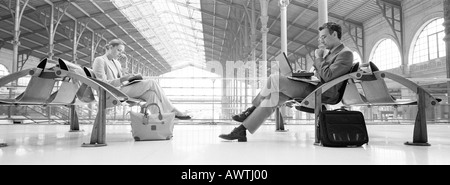 Businesspeople sitting in train station, b&w, panoramic view Stock Photo