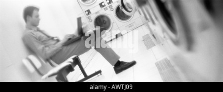 Man sitting and using laptop in laundrymat, b&w, panoramic view Stock Photo